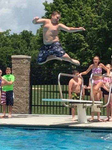 Boy jumping off a diving board into a swimming pool
