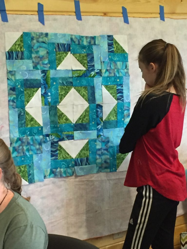 Girl standing in front of a quilt taped on a wall