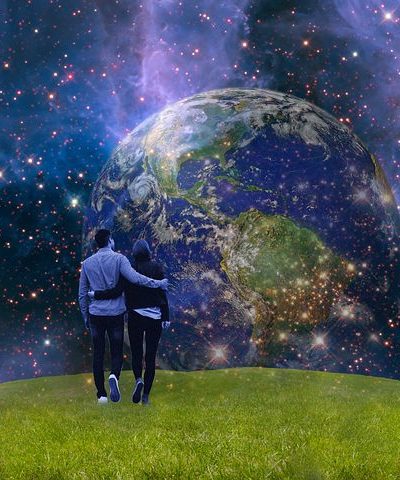 Two people standing on the edge of a grassy field overlooking the universe. 